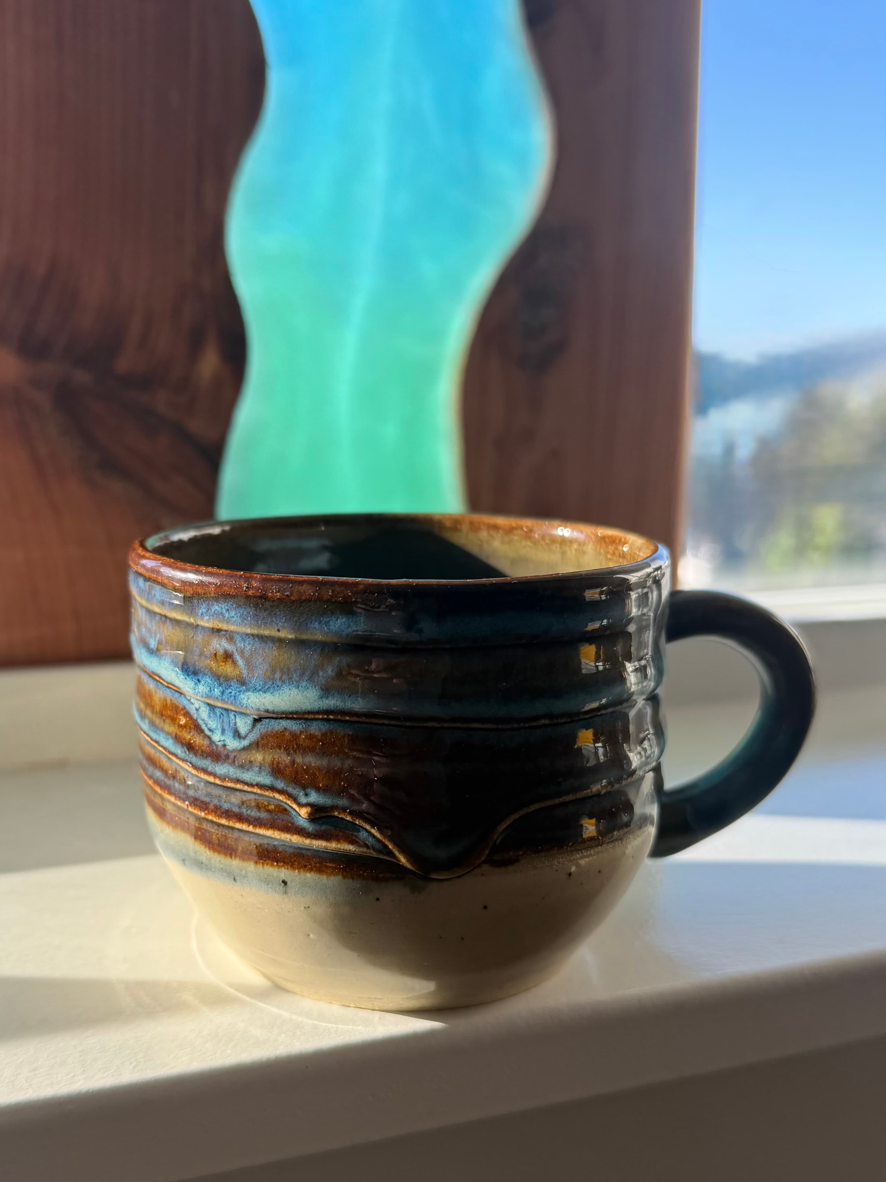 A tall banded mug resting on a sunlit windowsill