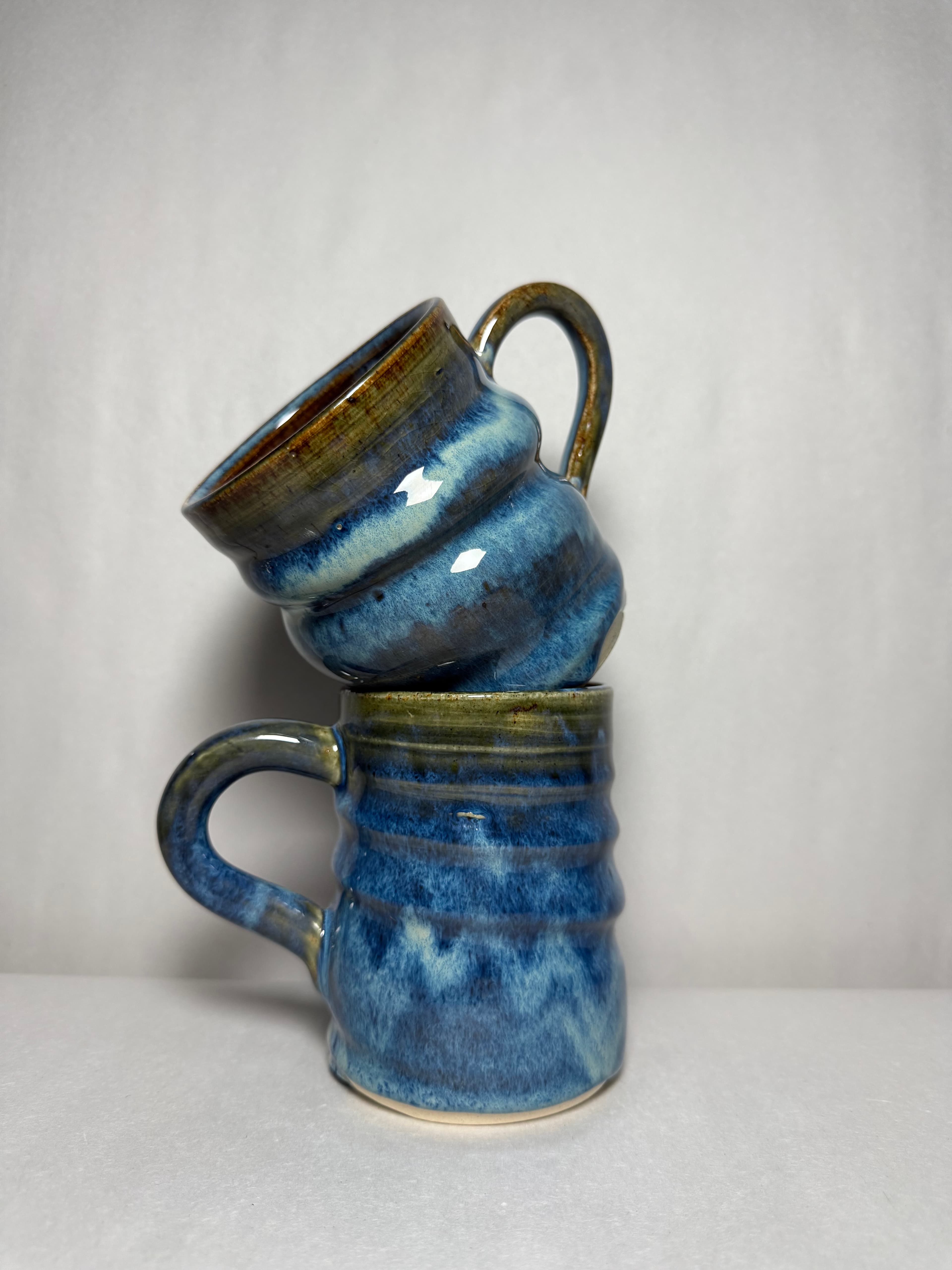 A pair of blue and green banded mugs resting together