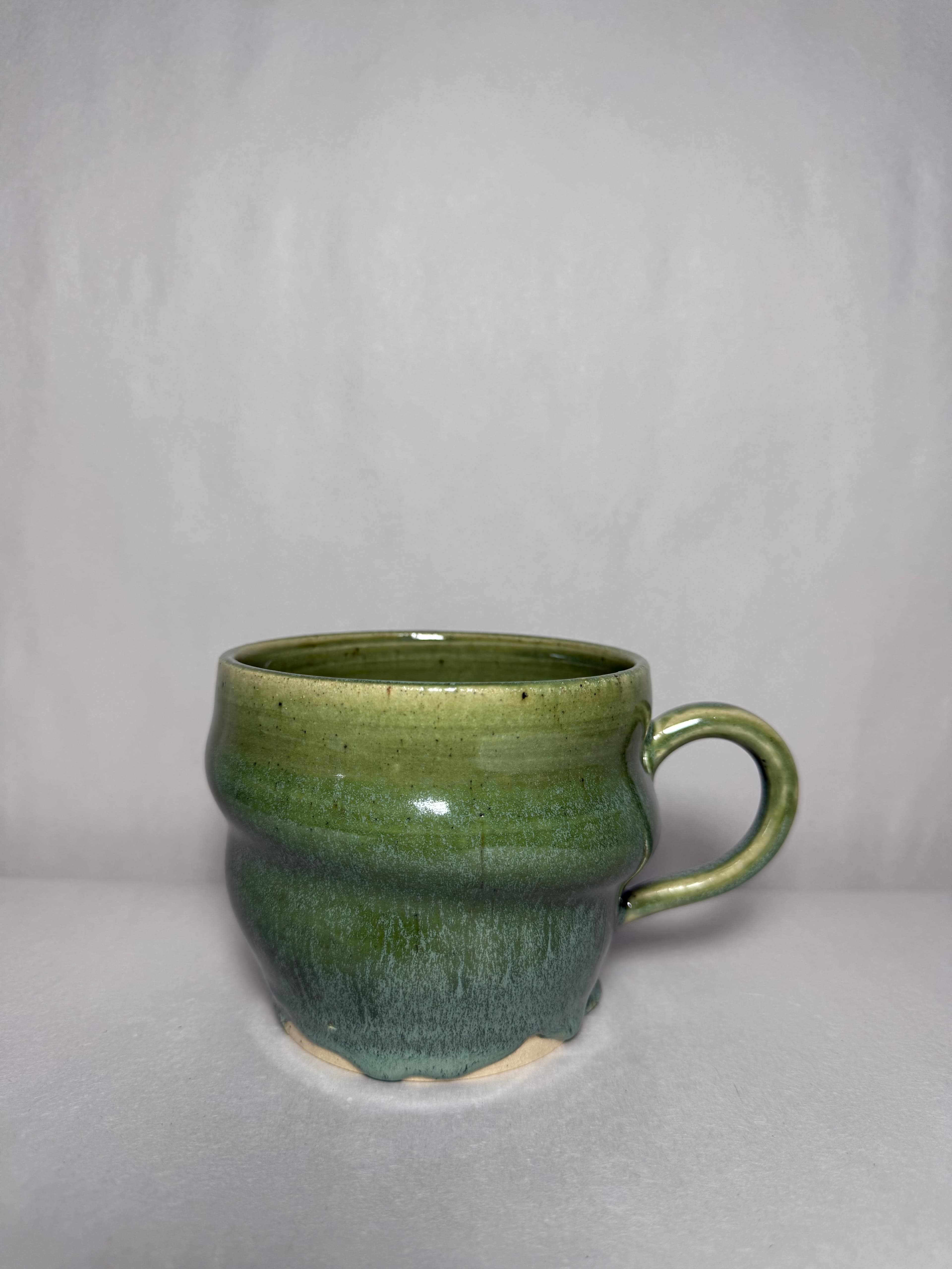 A glossy green mug photographed against a soft gray ground
