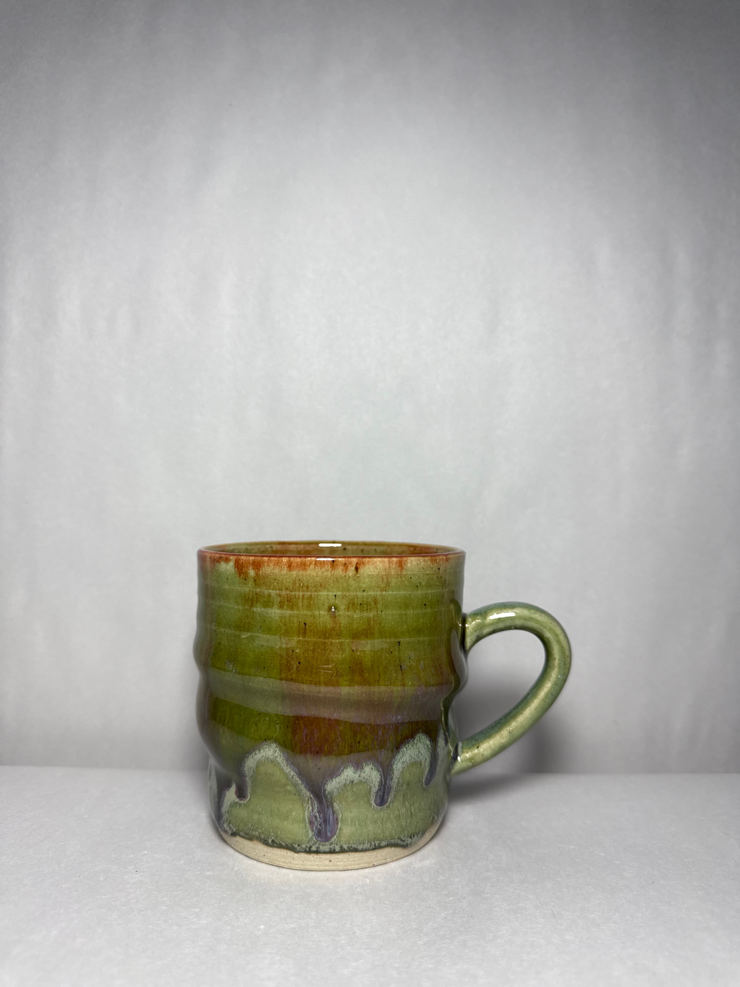 A green mug with red blush striations and a drip rim
