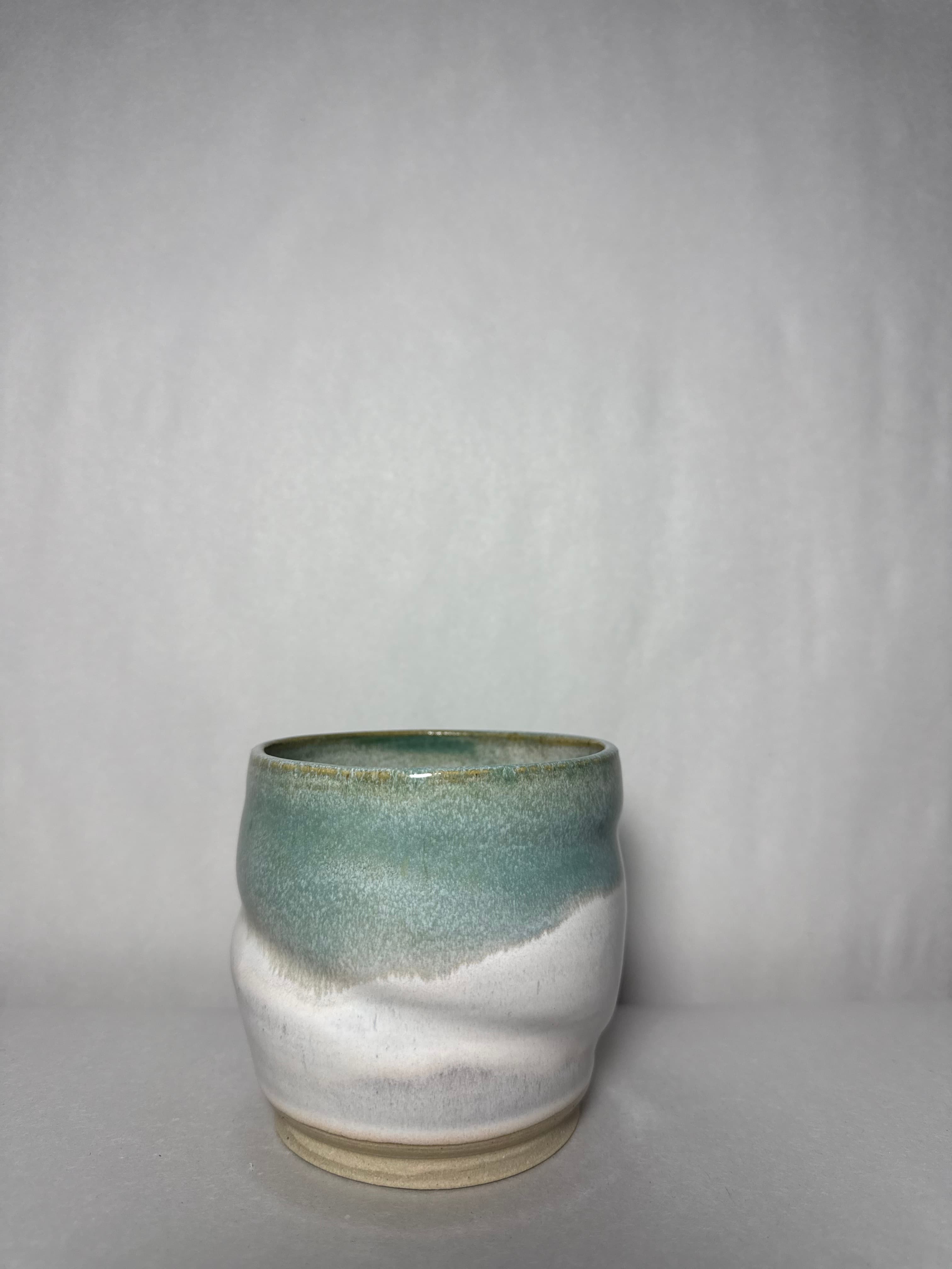 A celadon and white tumbler photographed on soft gray paper