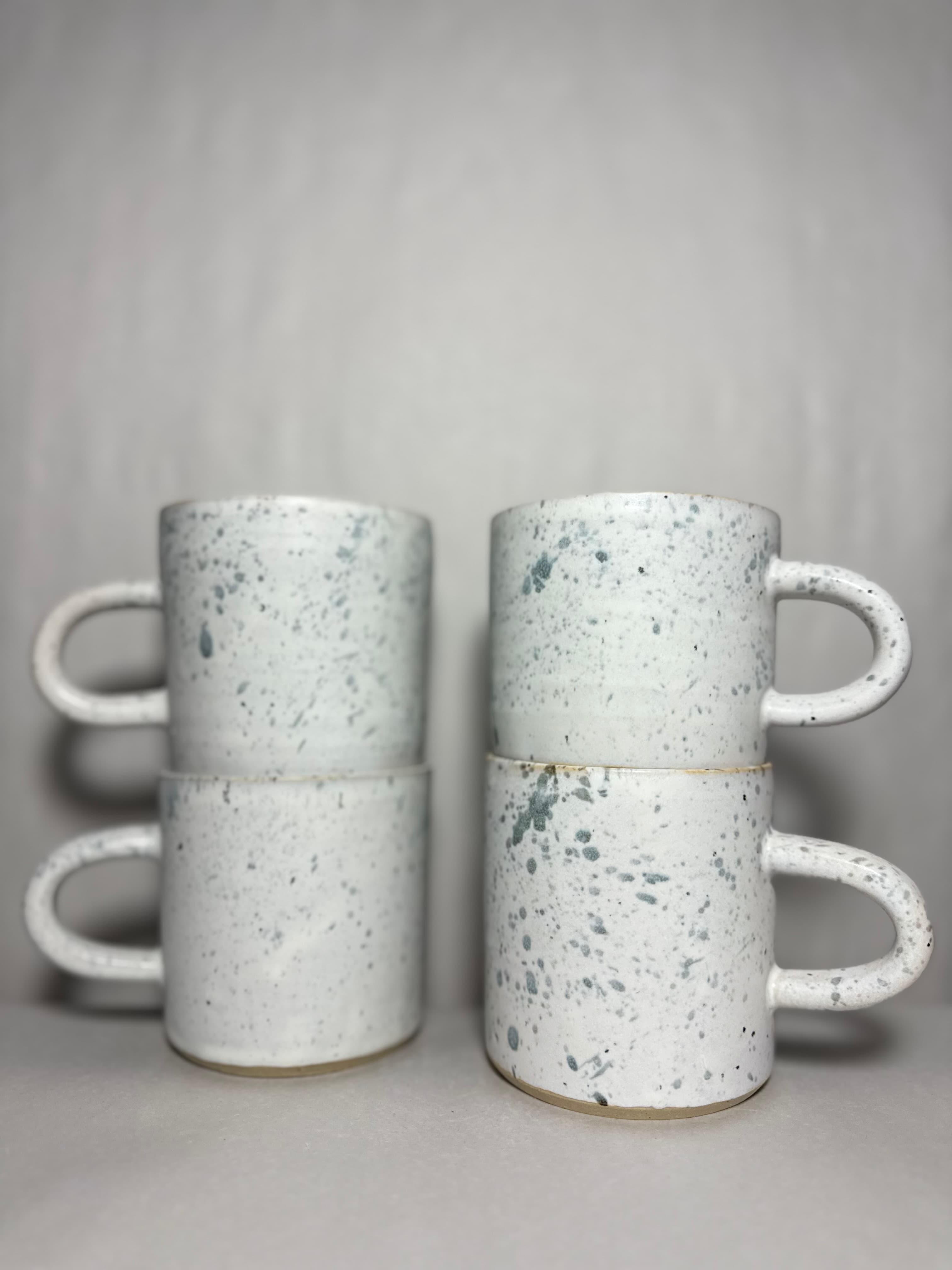 Four speckled white stoneware mugs stacked in two columns