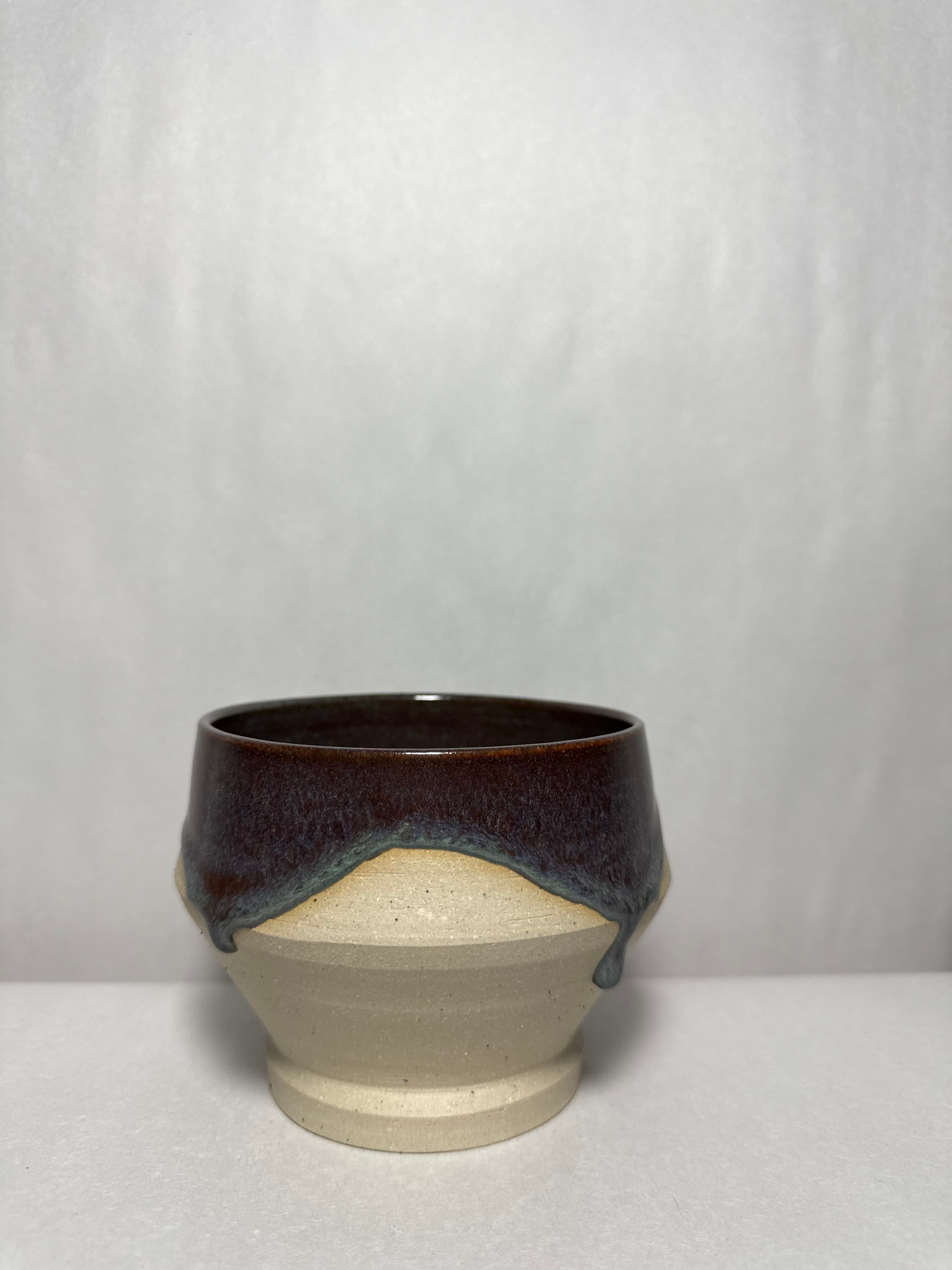 A raw stoneware bowl with a dark drip glaze pooling over the rim