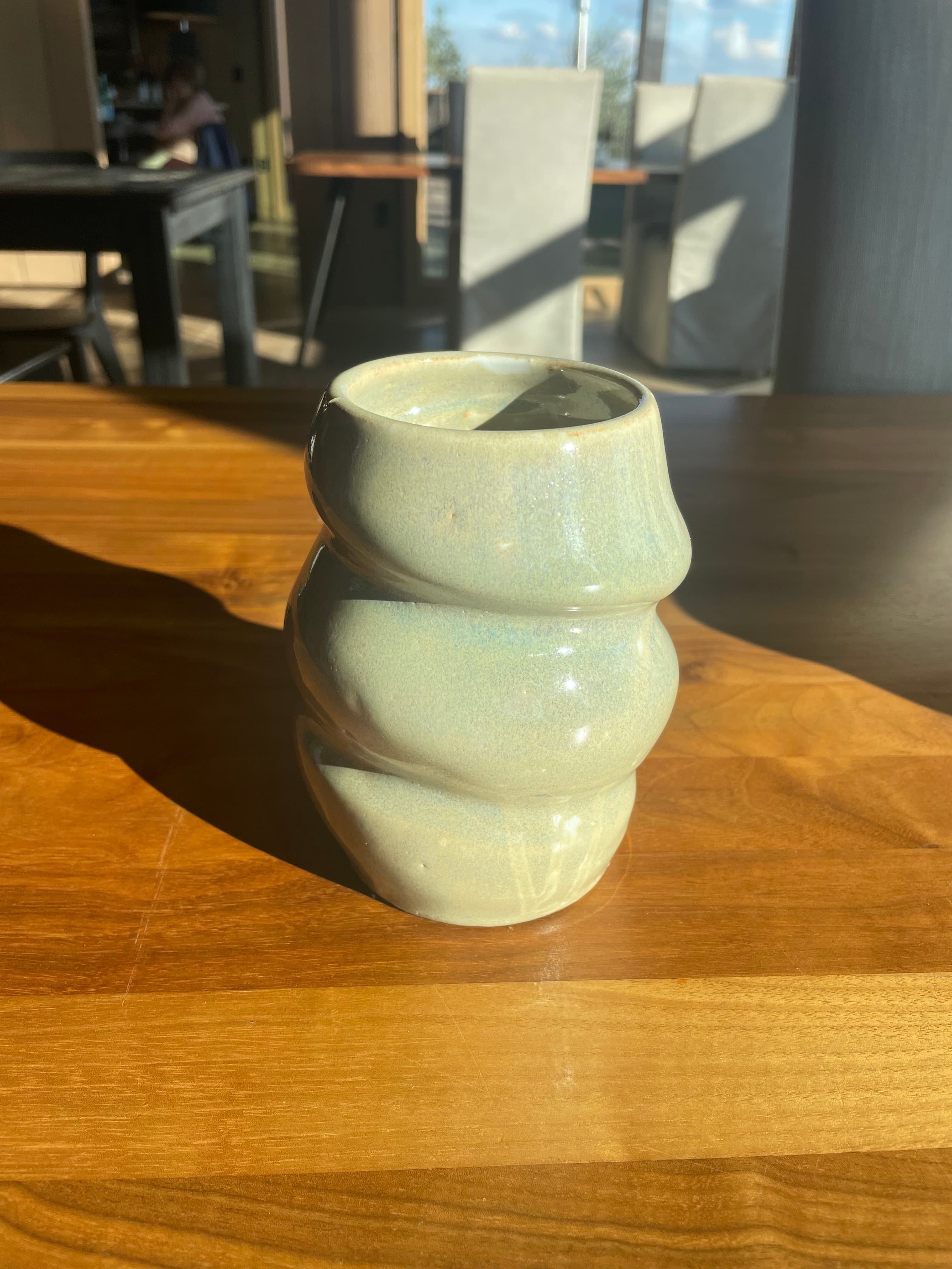 A mint celadon ridged vase photographed on a walnut surface